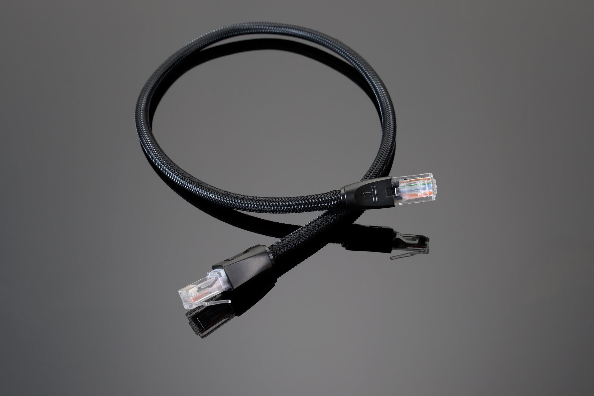 A Transparent Audio Ethernet cable coiled on a dark reflective surface, displaying both modular connectors at each end. Ideal for your high-performance networking solutions.