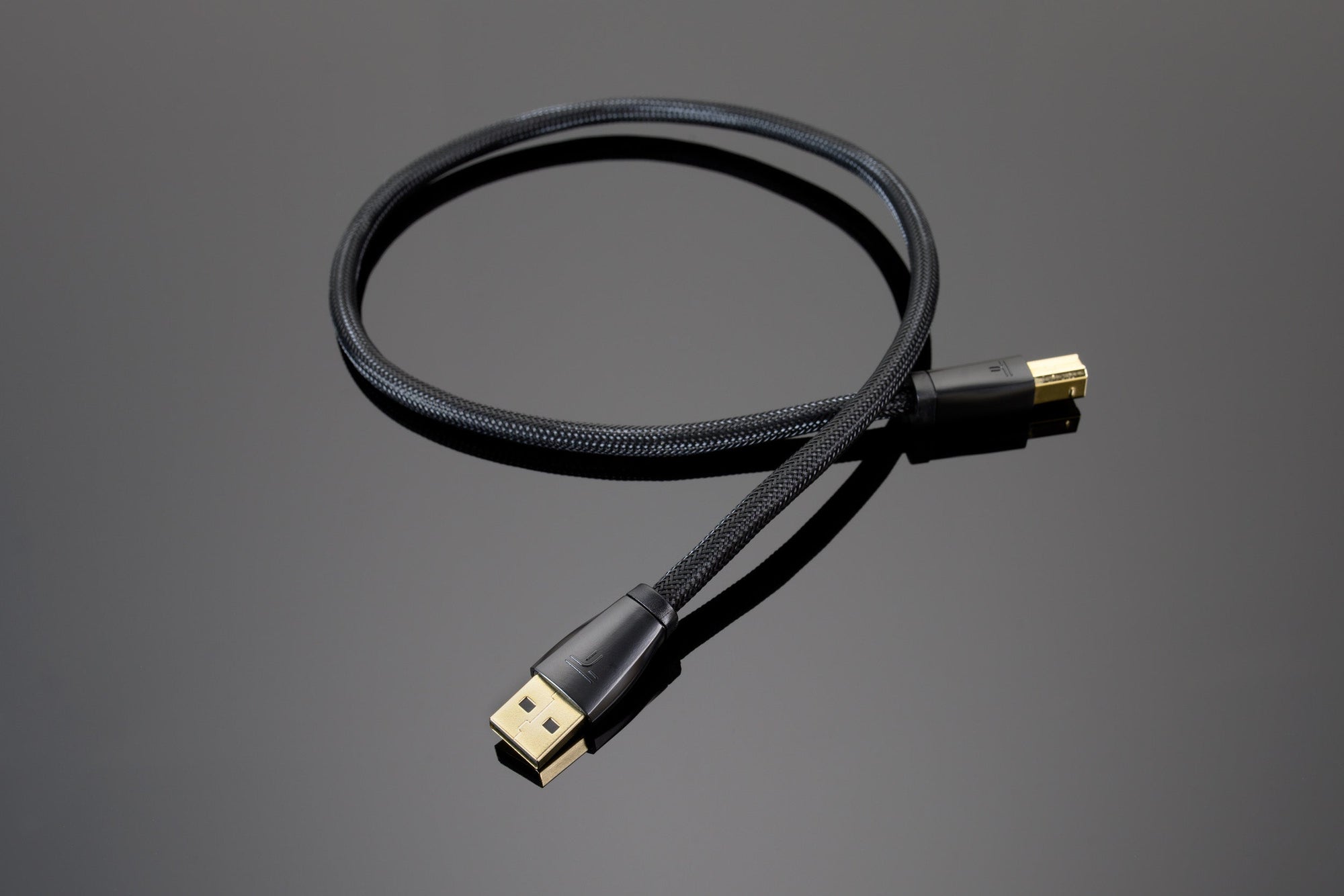 A Transparent Audio Transparent USB Digital cable with gold-plated connectors is coiled on a reflective surface, offering a premium digital solution.