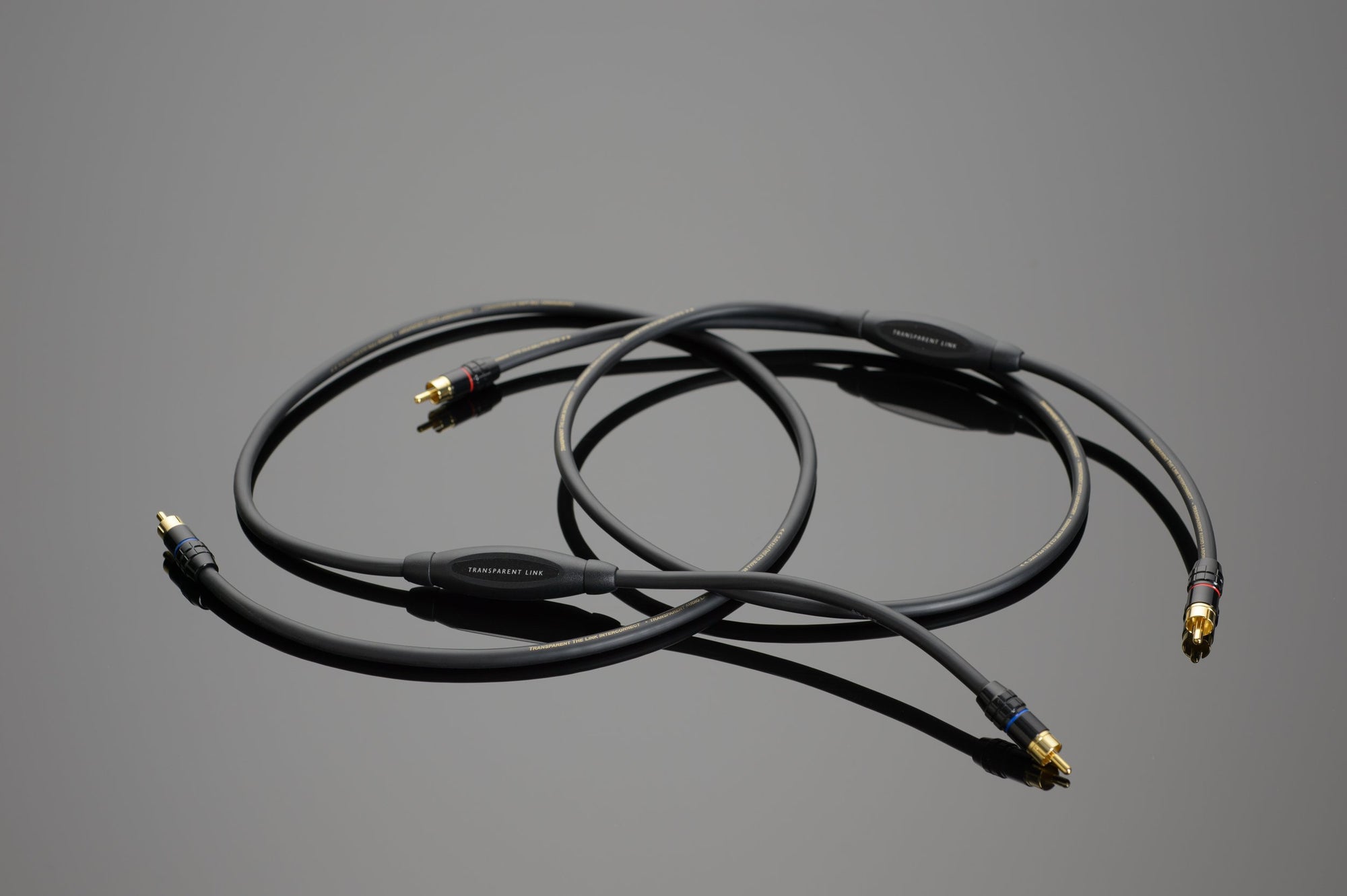 Image of two coiled Link RCA Interconnects with connectors on a reflective surface, ideal for a Transparent Audio system and dynamic sound quality.