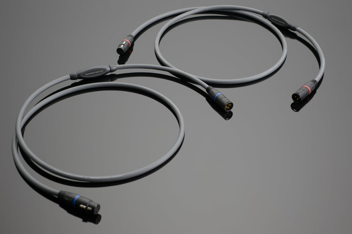 Two MusicLink Balanced Interconnects by Transparent Audio, featuring black connectors, are coiled and arranged side by side on a reflective surface.